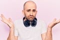 Young handsome bald man listening to music using headphones clueless and confused with open arms, no idea and doubtful face Royalty Free Stock Photo