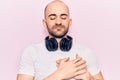Young handsome bald man listening to music using headphones smiling with hands on chest, eyes closed with grateful gesture on face Royalty Free Stock Photo