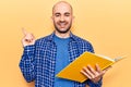 Young handsome bald man reading book smiling happy pointing with hand and finger to the side Royalty Free Stock Photo