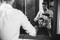 Young handsome barber making haircut for attractive man in barbershop