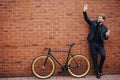 Young handsome bearded business man in suit and glasses wave with hands hello gesture for greatings standing near his bicycle on