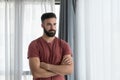 Young handsome bearded depressed man standing alone and looking through the window felling depression and anxiety after his girlfr