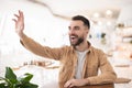 Young handsome bearded man waving greeting his friend while sitting in the cafe , body language concept