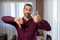 Young handsome bearded man wearing purple shirt doing thumbs up and down, disagree and agree expression Royalty Free Stock Photo