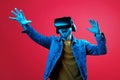 Young handsome bearded man wearing virtual reality goggles in studio on red background in neon light. Smartphone using