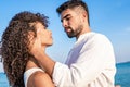 Young handsome bearded man in white shirt grabs his curly hispanic woman forcefully holding her head in his hands with serious