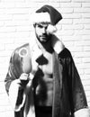 Young handsome bearded christmas man with stylish beard in red santa claus hat and coat with muscular bare torso