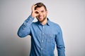 Young handsome blond man with beard and blue eyes wearing casual denim shirt doing ok gesture with hand smiling, eye looking Royalty Free Stock Photo