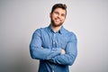Young handsome blond man with beard and blue eyes wearing casual denim shirt happy face smiling with crossed arms looking at the Royalty Free Stock Photo