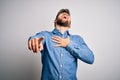 Young handsome blond man with beard and blue eyes wearing casual denim shirt laughing at you, pointing finger to the camera with Royalty Free Stock Photo