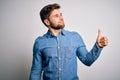 Young handsome blond man with beard and blue eyes wearing casual denim shirt Looking proud, smiling doing thumbs up gesture to the Royalty Free Stock Photo