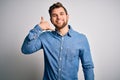 Young handsome blond man with beard and blue eyes wearing casual denim shirt smiling doing phone gesture with hand and fingers Royalty Free Stock Photo