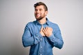 Young handsome blond man with beard and blue eyes wearing casual denim shirt smiling with hands on chest with closed eyes and Royalty Free Stock Photo