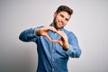 Young handsome blond man with beard and blue eyes wearing casual denim shirt smiling in love doing heart symbol shape with hands Royalty Free Stock Photo