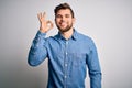 Young handsome blond man with beard and blue eyes wearing casual denim shirt smiling positive doing ok sign with hand and fingers Royalty Free Stock Photo