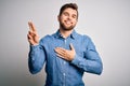 Young handsome blond man with beard and blue eyes wearing casual denim shirt smiling swearing with hand on chest and fingers up, Royalty Free Stock Photo