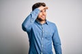 Young handsome blond man with beard and blue eyes wearing casual denim shirt very happy and smiling looking far away with hand Royalty Free Stock Photo