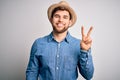 Young handsome blond man with beard and blue eyes wearing denim shirt and summer hat smiling with happy face winking at the camera Royalty Free Stock Photo