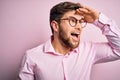 Young handsome blond man with beard and blue eyes wearing pink shirt and glasses very happy and smiling looking far away with hand Royalty Free Stock Photo