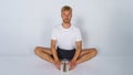 Young, handsome blond man in casual T-shirt and dark pants on white background doing stretches with eyes closed and concentrated Royalty Free Stock Photo