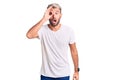 Young handsome blond man wearing casual t-shirt doing ok gesture with hand smiling, eye looking through fingers with happy face Royalty Free Stock Photo