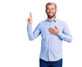 Young handsome blond man wearing elegant shirt smiling swearing with hand on chest and fingers up, making a loyalty promise oath Royalty Free Stock Photo