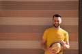 A young, handsome, blue-eyed, bearded man with a yellow T-shirt holds a hat in his hands. In the background a wall in shades of Royalty Free Stock Photo