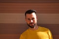 A young, handsome, blue-eyed, bearded man with a yellow T-shirt holds a hat in his hands. In the background a wall in shades of Royalty Free Stock Photo