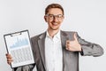 Young handsome brunette man in glasses in a suit smiles and shows thumbs up with business documents and graphs on white isolated Royalty Free Stock Photo