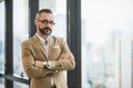Young handsome business bearded man standing near window with arms crossed in office work place Royalty Free Stock Photo