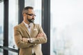 Young handsome business bearded man standing near window with arms crossed in office work place Royalty Free Stock Photo