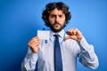 Young handsome business man with beard holding id card identification over blue background with angry face, negative sign showing Royalty Free Stock Photo