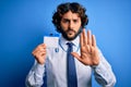 Young handsome business man with beard holding id card identification over blue background with open hand doing stop sign with Royalty Free Stock Photo