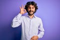 Young handsome business man with beard wearing shirt standing over purple background smiling positive doing ok sign with hand and Royalty Free Stock Photo