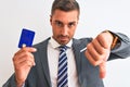 Young handsome business man holding credit card over isolated background with angry face, negative sign showing dislike with Royalty Free Stock Photo