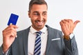 Young handsome business man holding credit card over isolated background pointing and showing with thumb up to the side with happy Royalty Free Stock Photo
