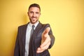 Young handsome business man over yellow isolated background smiling friendly offering handshake as greeting and welcoming Royalty Free Stock Photo