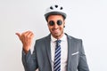 Young handsome business man wearing bike helmet and sunglasses over isolated background pointing and showing with thumb up to the Royalty Free Stock Photo