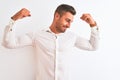 Young handsome business man wearing elegant shirt over isolated background showing arms muscles smiling proud