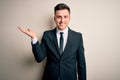 Young handsome business man wearing elegant suit and tie over isolated background smiling cheerful presenting and pointing with Royalty Free Stock Photo