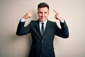 Young handsome business man wearing elegant suit and tie over isolated background smiling pointing to head with both hands finger, Royalty Free Stock Photo