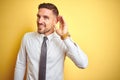 Young handsome business man wearing elegant white shirt over yellow isolated background smiling with hand over ear listening an Royalty Free Stock Photo