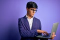 Young handsome business man wearing glasses working using laptop over purple background with a confident expression on smart face Royalty Free Stock Photo