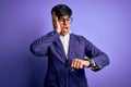 Young handsome business man wearing jacket and glasses over isolated purple background Looking at the watch time worried, afraid Royalty Free Stock Photo