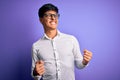 Young handsome business man wearing shirt and glasses over isolated purple background excited for success with arms raised and Royalty Free Stock Photo