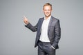 Young handsome businessman with beaming smile pointing with finger away on gray background