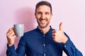 Young handsome businessman drinking mug of coffee over isolated pink background smiling happy and positive, thumb up doing Royalty Free Stock Photo