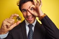 Young handsome businessman holding bitcoin standing over isolated yellow background with happy face smiling doing ok sign with Royalty Free Stock Photo