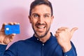 Young handsome businessman holding credit card over isolated pink background pointing thumb up to the side smiling happy with open Royalty Free Stock Photo