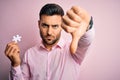 Young handsome businessman holding piece of puzzle over isolated pink background with angry face, negative sign showing dislike Royalty Free Stock Photo